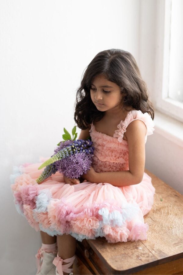 Girl in a pink tulle dress with rainbow colours and white knee-high socks holding flowers