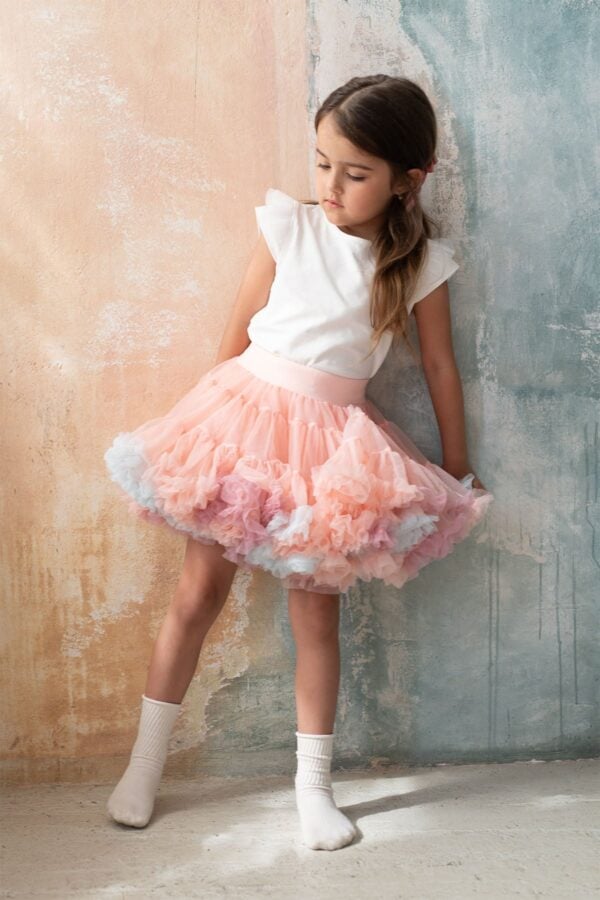 Girl in a pink tulle skirt with rainbow ruffles, white knee-high socks and a white strappy top