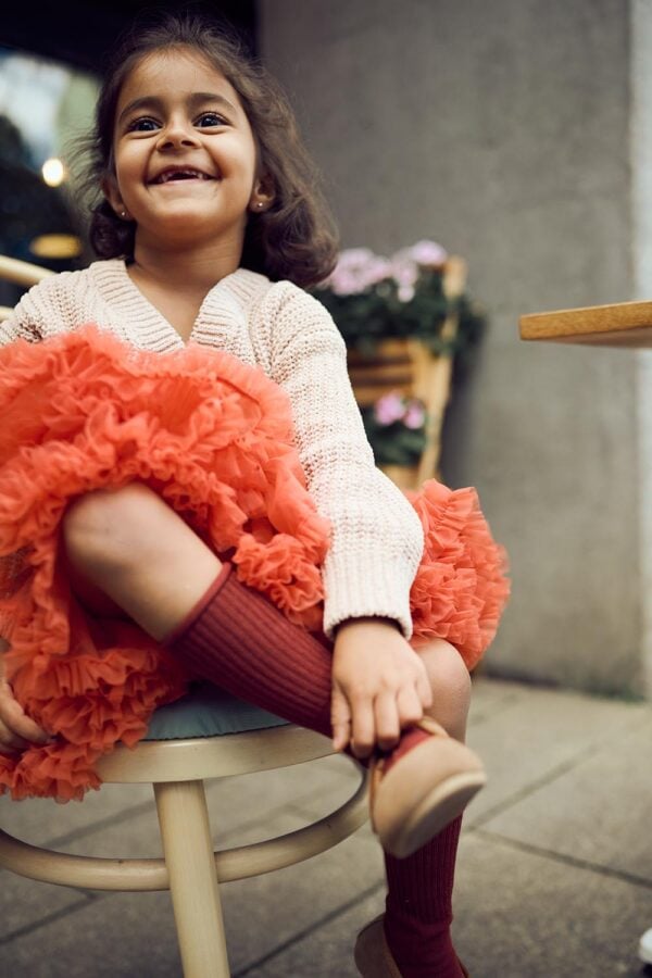 Falda de tul en color naranja con volantes, para niñas, combinada con calcetas marrones y un suéter claro. Tallas disponibles: 98/104, 110/116, 122/128, 134, 86/92