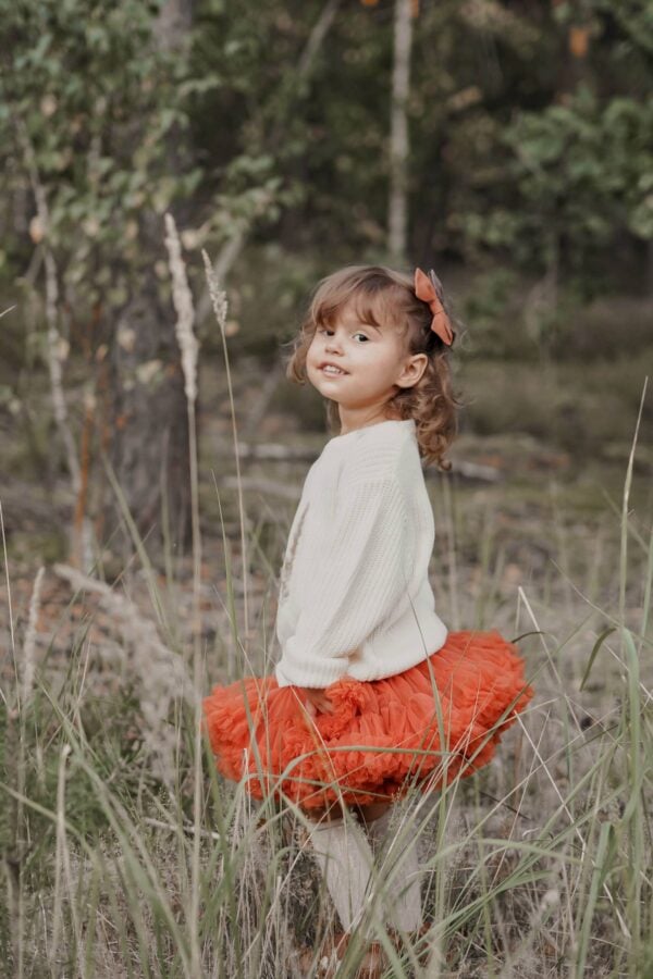 Falda de tul naranja brillante para niñas, combinada con un suéter blanco, en un entorno natural. Tallas disponibles: 98/104, 110/116, 122/128, 134, 86/92