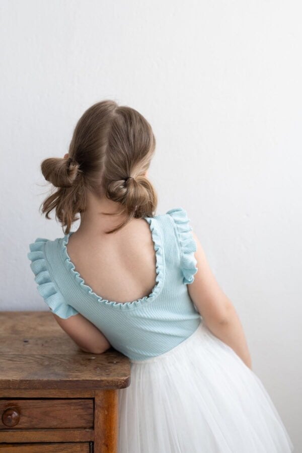 Niña de pie con top sin mangas azul y falda larga blanca de tul para niña