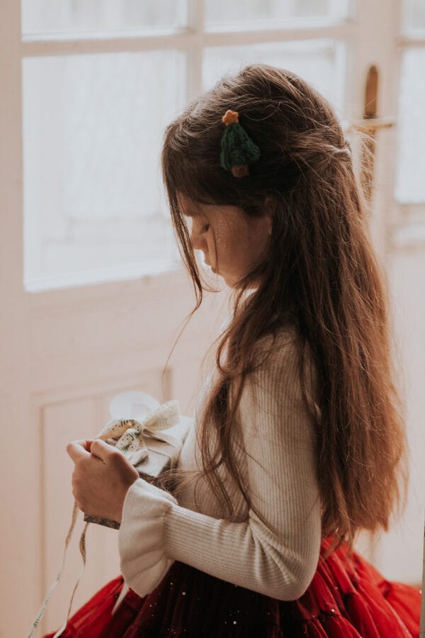 Une jeune fille aux cheveux longs, vêtue d'un chemisier blanc et d'une jupe rouge, tient un cadeau avec un nœud.