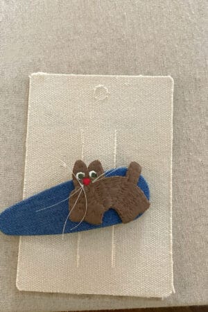 Haarnadel für ein Mädchen mit einer gestickten braunen Katze auf blauem Hintergrund.
