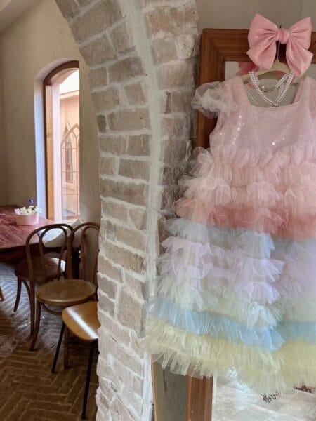 Kleid für ein Mädchen in Rosa und Blau, verziert mit Tüllrüschen, aufgehängt mit einer rosa Schleife. Verfügbare Größen: 104/110, 110/116, 122/128, 134, 140