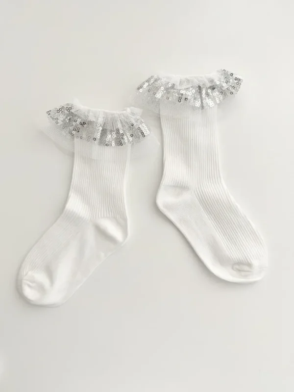 Chaussettes pour une fille, blanches avec du tulle et des paillettes argentées sur le bord.
