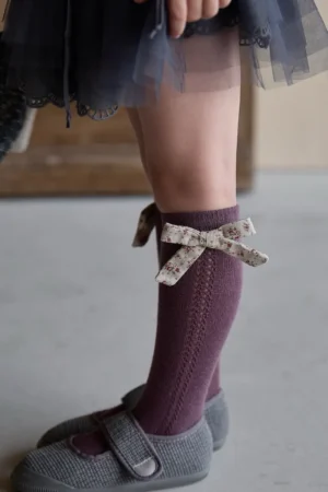 Pflaumenfarbene Socken mit einer dekorativen Blumenschleife, perfekt für ein Mädchen.