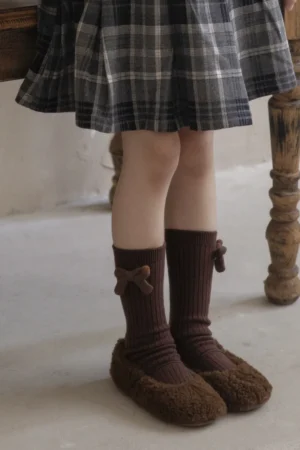 Calcetines marrones de canalé con lazos combinados con zapatillas marrones de felpa, bajo una falda de cuadros escoceses
