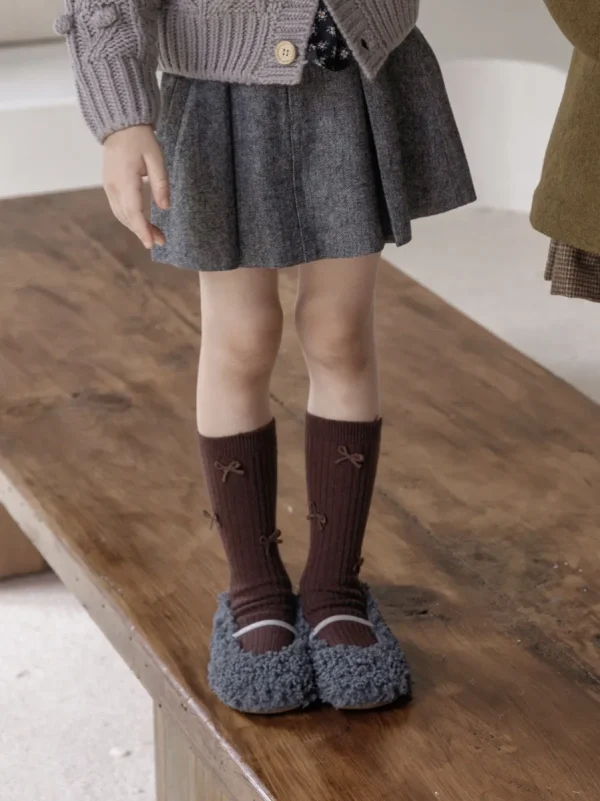 Girl's brown ribbed socks with small bows, paired with a gray skirt and cozy shoes.