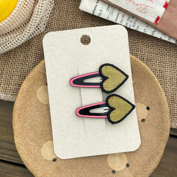 Heart-shaped hair clips, gold with a pink accent, for a girl.