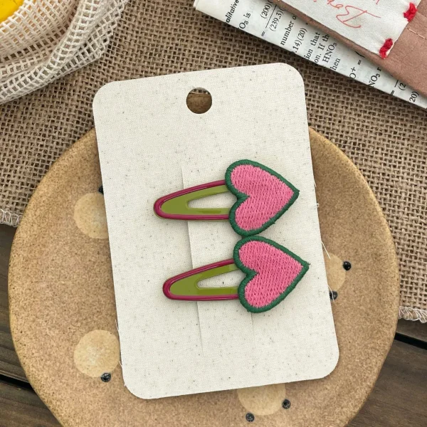 Heart-shaped hair clips, pink with green trim, for a girl.