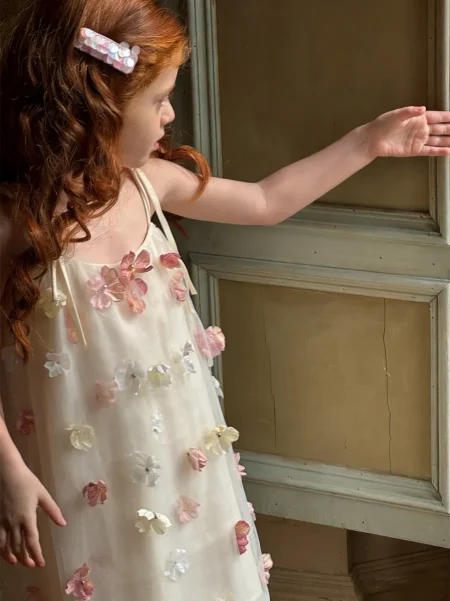 Light-coloured girl’s dress with floral appliqués in shades of pink and white. Available sizes: 98/104, 104/110, 110/116, 122/128, 134