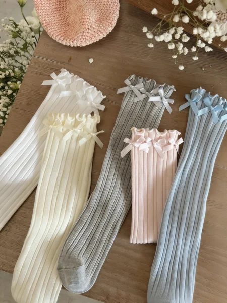 Calzini a coste in tonalità bianco, grigio, rosa e azzurro con fiocchi, per bambina.