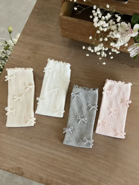 Calzini per bambina in crema, bianco, grigio e rosa, con fiocchi decorativi.