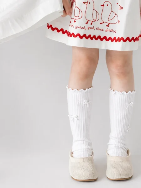Calzini bianchi a coste da bambina con fiocchi, ideali con un vestito.