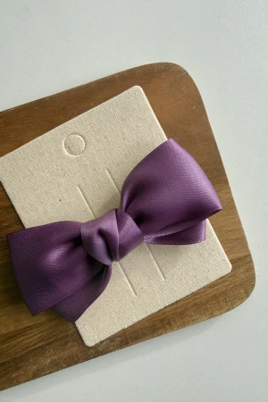 Dekorative violette Schleife auf cremefarbener Karte auf einem Holzbrett.