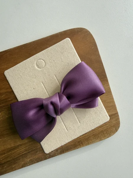 Dekorative violette Schleife auf cremefarbener Karte auf einem Holzbrett.