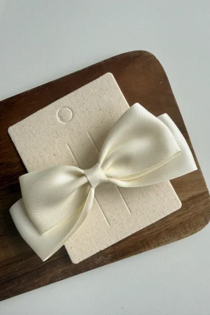 White bow for a girl on a beige stand, placed on a wooden board.