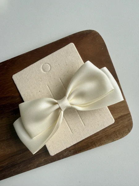 Fiocco bianco per bambina su base beige, appoggiato su una tavola di legno.