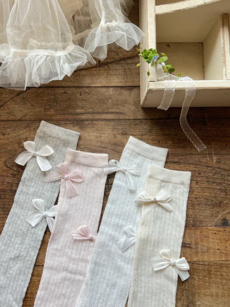 Calzini da bambina grigi, rosa, bianchi e crema, decorati con fiocchi.