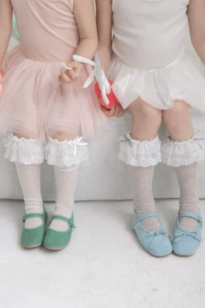 Mädchenkleider in Rosa und Weiß, Spitzensocken sowie grüne und blaue Schuhe.