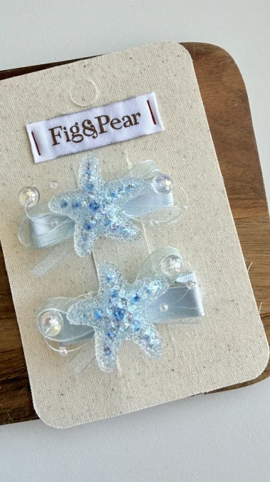 Hair clips shaped like pale blue stars, with glittery details and a satin ribbon.