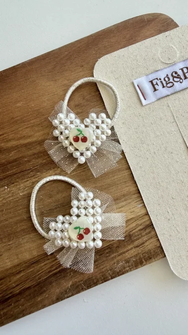 Two heart-shaped hair ties for a girl, decorated with pearls and a cherry motif.