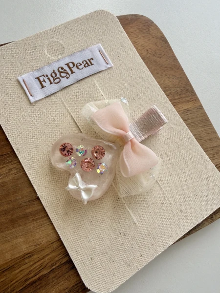 Decorative heart-shaped brooch with pink stones and a bow for a girl.