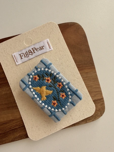 Blue-toned brooch with an embroidered yellow bird and flowers for a girl.