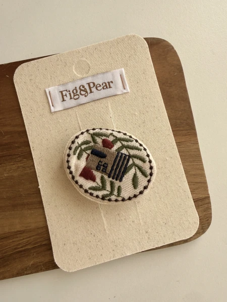 Girl’s necklace with embroidered house and plants in soft colours.