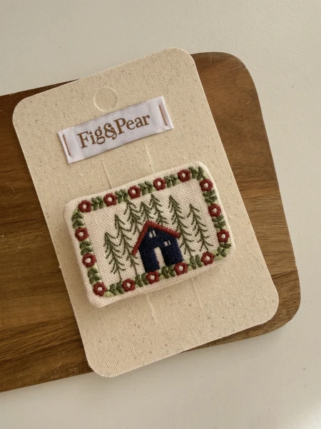 Embroidered patch with a house and trees in navy, red and green.